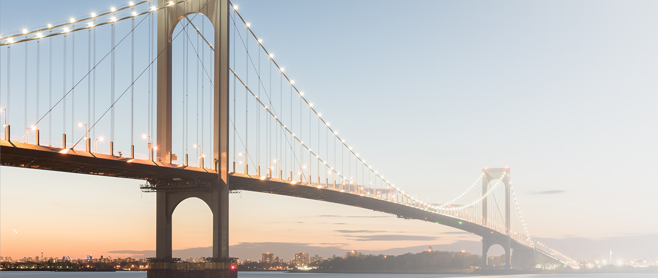 Illuminated suspension bridge at dusk with reflections on the water, under a clear evening sky