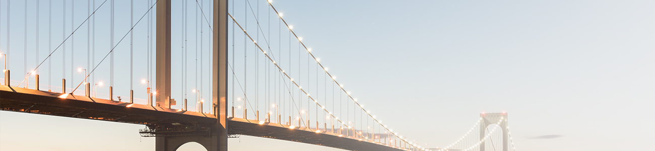 Illuminated suspension bridge at dusk with reflections on the water, under a clear evening sky